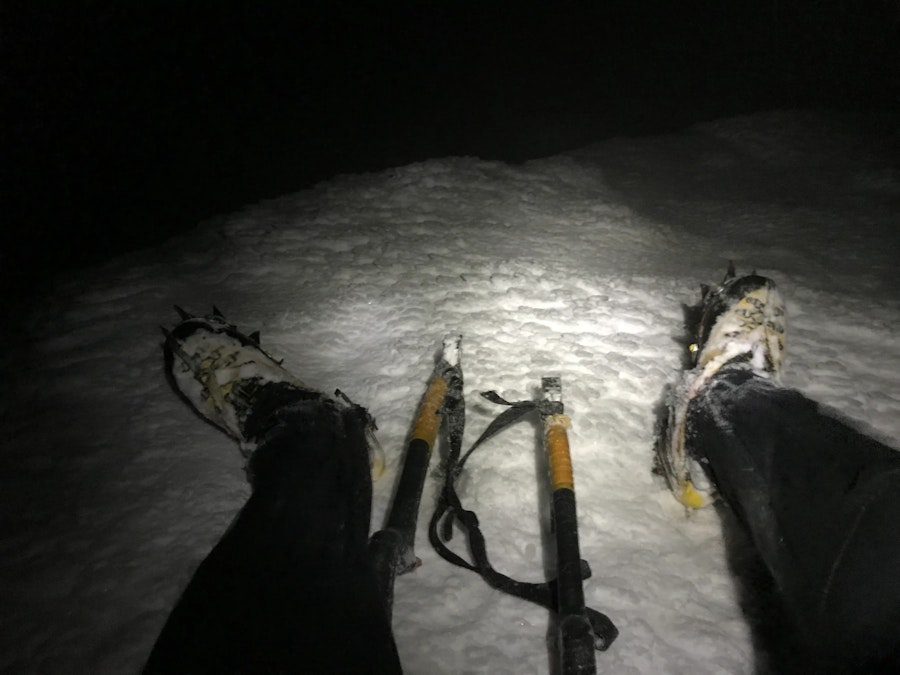 A photo, taken by a mountaineer of himself with the camera pointed down at his boots while sitting in the snow on a mountain.