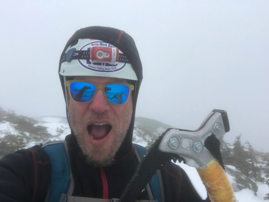 A mountaineer posing on a sumit holding an ice axe.