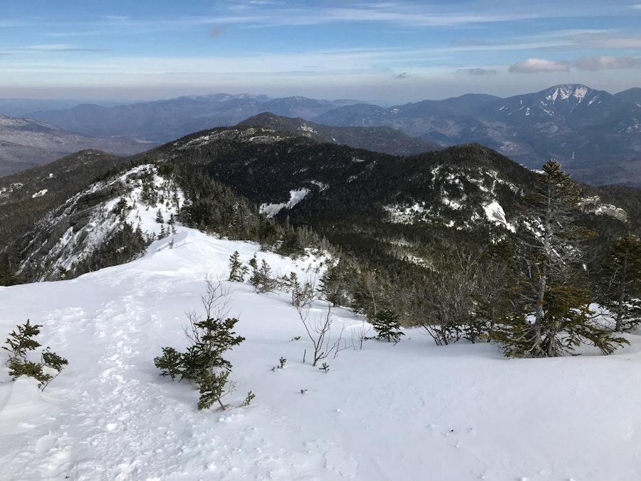 A snowy mountain ridge in the midst of snow and tree covered mountains.