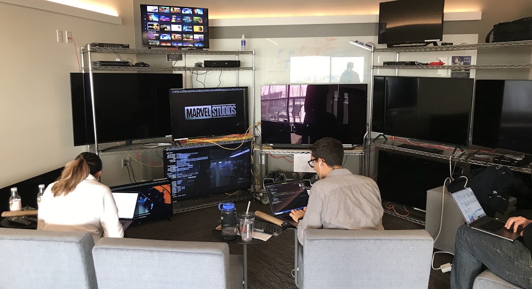 A small crew of software engineers on their laptops in front of multiple monitors and cables.