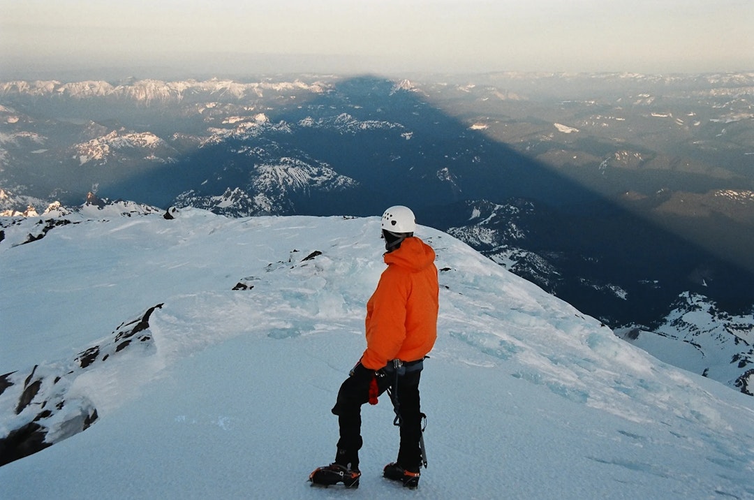A man stands on top of a mountain with the landscape stretching far below him.