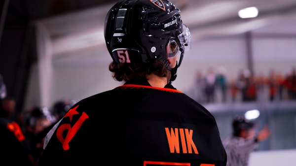Teenage girls and boys playing hockey wearing team uniforms and helmets.