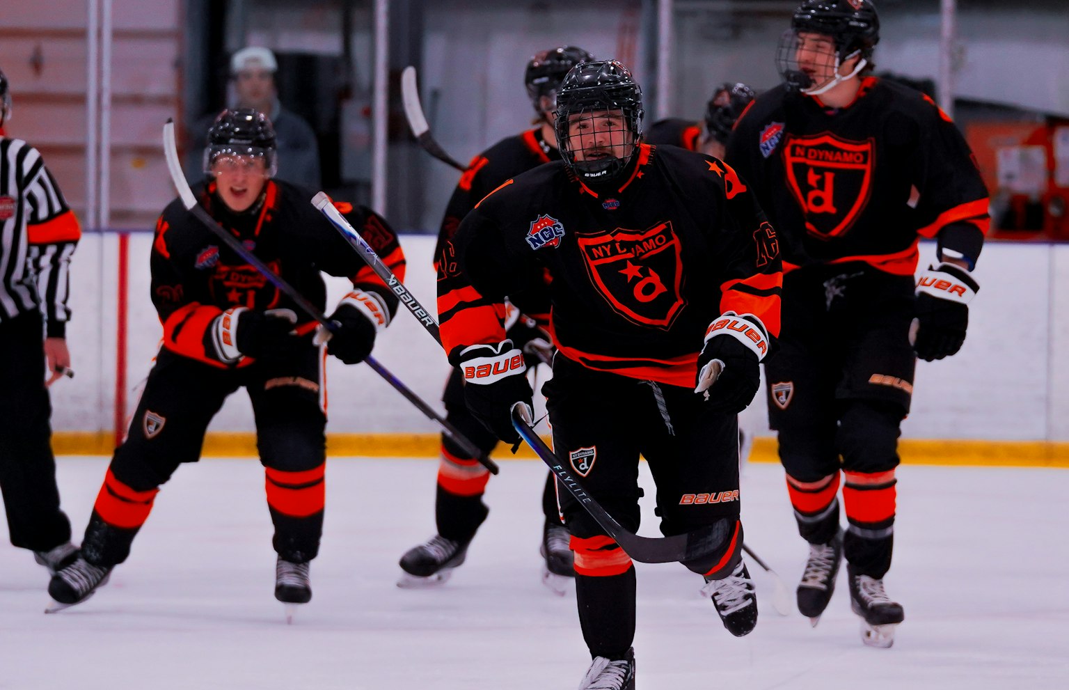 Four NY Dynamo hockey players celebrate by skating directly at the camera after scoring a goal.