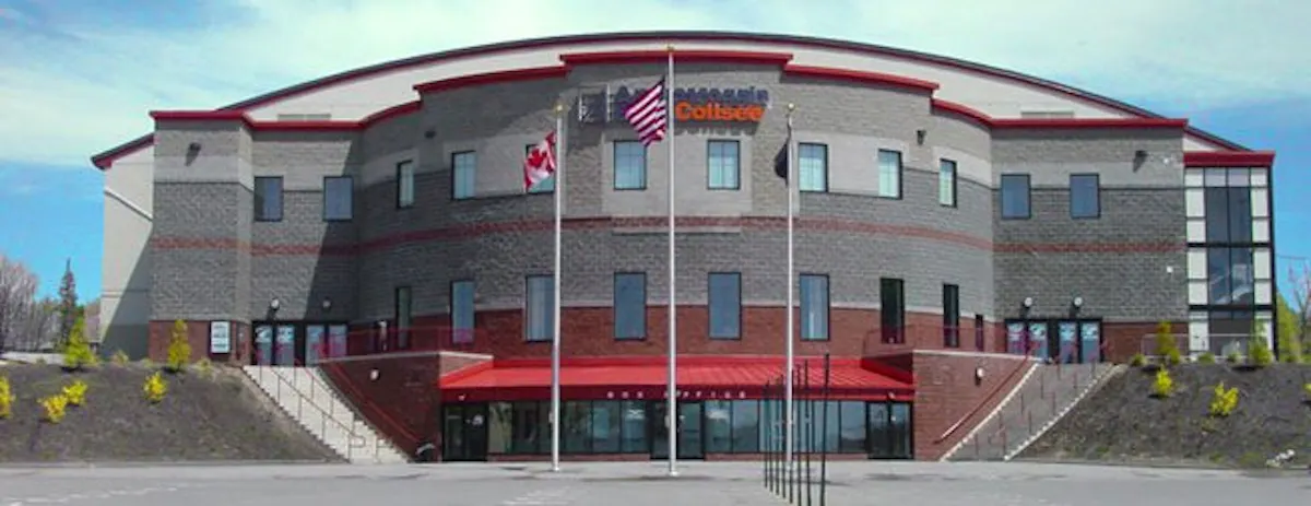 Front exterior of the Colis&eacute;e sports and events arena, featuring a curved brick fa&ccedil;ade with red trim, broad entrance stairs, and Canadian and American flags.