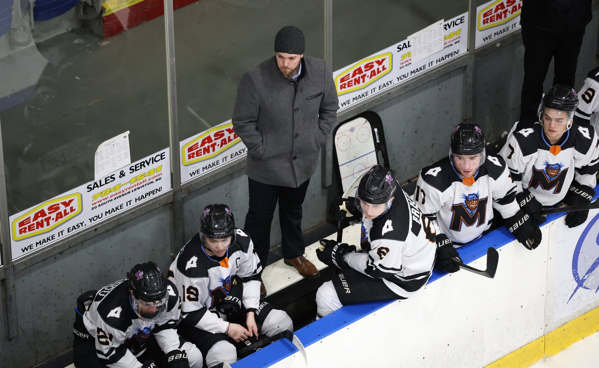 MAINEiacs players and a coach on the bench during a game